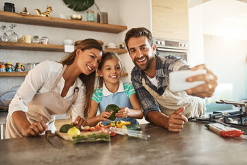 Poster - This calls for a selfie. Shot of a happy young family posing for a selfie while cooking together in their kitchen.