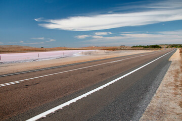 Landscape with a straight line of the road going into the distance in the desert with a background of a pink salt lake and a blue sky