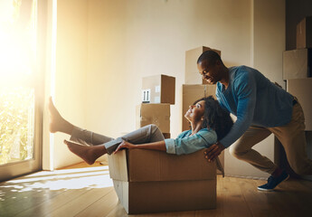 Go faster. Shot of a cheerful young man pushing his girlfriend around in a cardboard box at home during moving day.