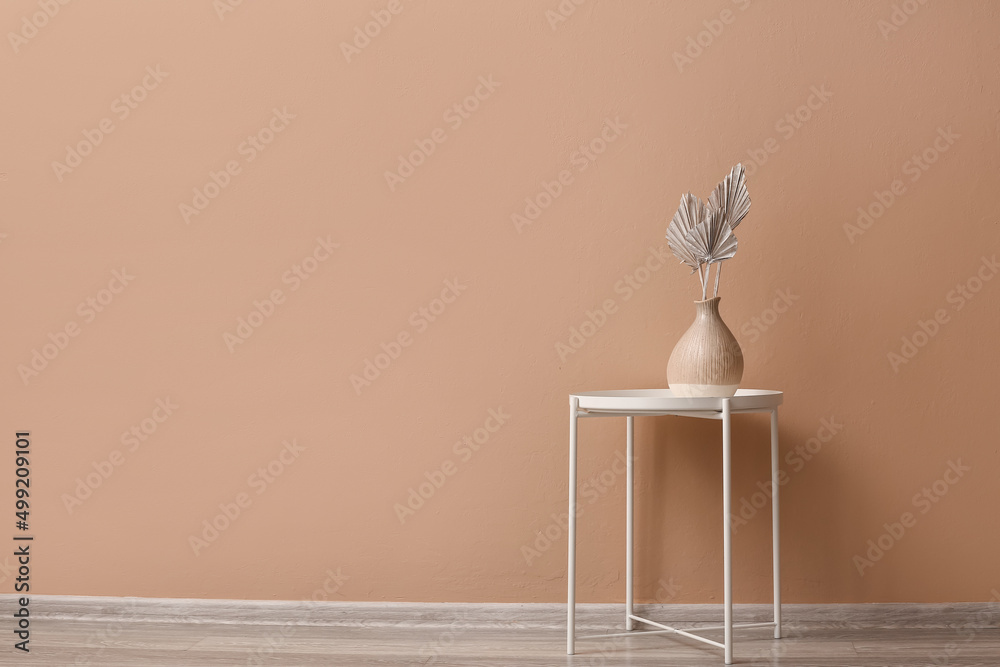 Vase with dried flowers on table near beige wall