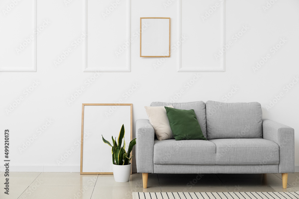 New sofa, blank posters and houseplant near white wall