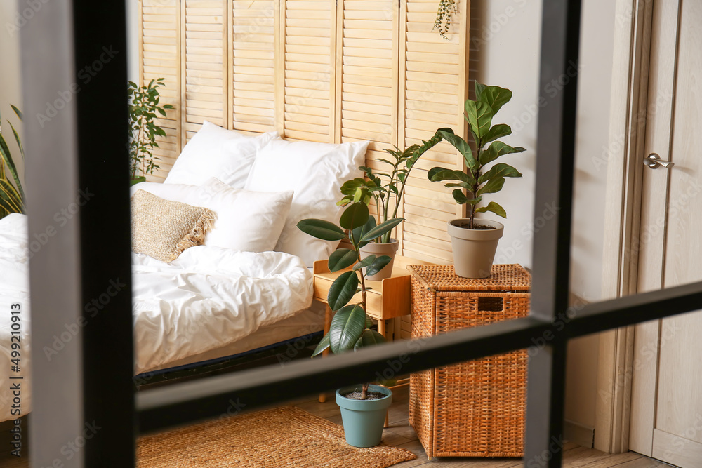 Interior of light bedroom with houseplants and folding screen