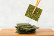 Wooden board with tasty seaweed sheets on light background
