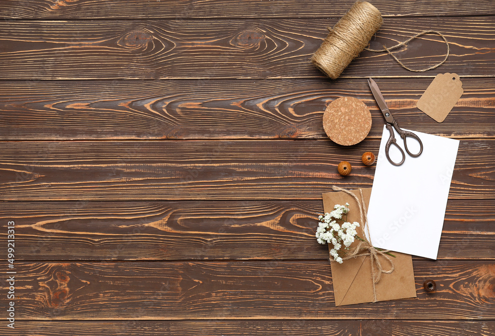 Envelope with card, scissors, flowers and rope on wooden background