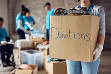Close Up Of Woman Holds Cardboard Box Filled With Donated Clothes While Volunteering At Charity Center.