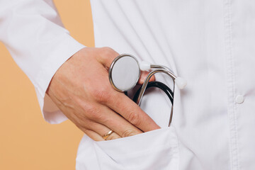 No face, detail of doctor's hands holding stethoscope on a beige background