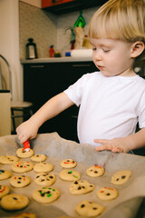 A little blond boy of two years old is cooking homemade cookies in the kitchen