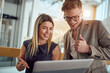 © luckybusiness - A young business woman is standing in the hallway and explaining a laptop content to her young male colleague. Business, people, company