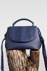 Blue leather handbag on wooden snag. Creative fashion minimal background.