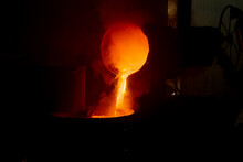 The Work Of The Foundry. Pouring Hot Metal From The Bucket Into Molds. Bright Red Metal, Smoke And Sparks Flying To The Sides