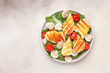 Wall Mural - Vegetarian salad with spinach leaves, cherry tomatoes, mushrooms and grilled halumi cheese in a plate on the table. Top View