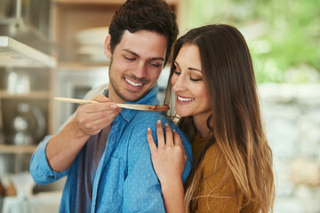 Poster - Tell me what you think.... Shot of a handsome young man giving his girlfriend a taste of what hes cooking.