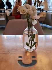 White flowers in a vase stand on a brown table