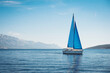 White yacht with blue sails in the sea against a background of blue sky and mountains