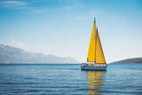 White yacht with yellow sails in the sea against a background of blue sky and mountains