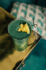 Sticker - green spirulina smoothie with pineapple on brass, gold table and teal background	
