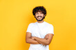© Kateryna - Happy positive indian or arabian curly-haired guy in basic white t-shirt, pointing fingers up at empty mockup space for advertising, announcement, standing on isolated orange background, smiling
