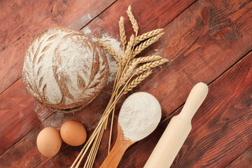 Round bread, 2 brown eggs, wheat ears, white flour in a light wooden spoon. Concept agricultural, farm natural products, ingredients for baking, harvest. Import Export.