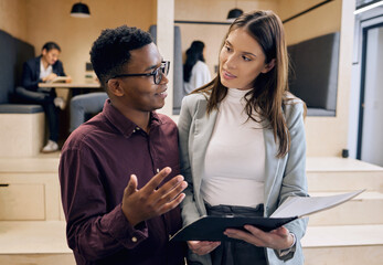 Poster - He values her opinion. Cropped shot of two young businesspeople looking over paperwork with their colleagues in the background.