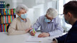 © TommyStockProject - Senior couple in safety mask signing on document in real estate agent office