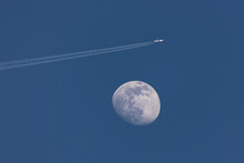Closeup Of The Waxing Moon And An Airplane Passing Close By, Leaving A Contrail  - Early Evening Capture Against Dark Blue Sky. Stuttgart, Germany April, 13, 2022