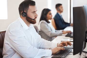 Wall Mural - Let me take a deeper look into this. Shot of a young call centre agent working in an office with his colleague in the background.