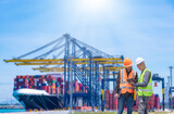 Engineer wearing uniform inspection and see detail on tablet with logistics container dock cargo yard with working crane bridge in shipyard with transport logistic import export background.