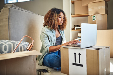 Poster - So much to do still. Shot of a focused young woman working on a laptop while seated on the floor and with boxes all around her at home.