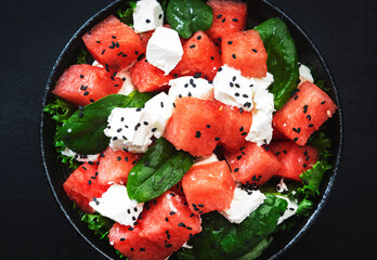 Wall Mural - Summer Watermelon juicy salad bowl with feta cheese, spinach and black sesame seed, dark table background, top view, negative space