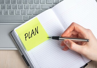 Poster - Woman hand closeup writing plans in notebook. Time management, organizing concept. Female sitting at table with laptop and taking notes. High quality photo