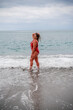 © svetograph - Woman in a bathing suit at the sea. A fat young woman in a red swimsuit enters the water during the surf