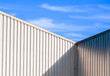 © Prapat - Sunlight and shadow on surface of corrugated steel wall of warehouse building against blue sky background in perspective view