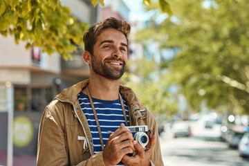 Sticker - His camera travels wherever he does. Shot of a happy tourist taking pictures while exploring a foreign city on his own.