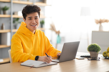 Wall Mural - Smiling asian man working on laptop and writing