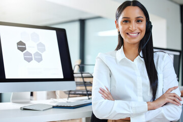 Some heroes wear headsets. Shot of an attractive young call centre agent sitting in the office with her arms crossed while wearing a headset.