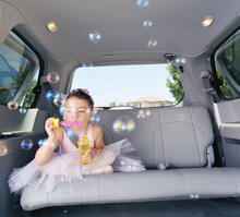 Girl (6-7) In Ballet Outfit Blowing Bubbles In Car