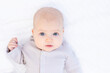 © Any Grant - portrait of a newborn baby girl in a cotton suit on a white bed at home lying and smiling, a place for text