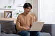 Entrepreneur handsome business asian man wear shirt sitting on couch working online with computer laptop smile happiness and relax at home office.Young male using social media.Small Business Startup