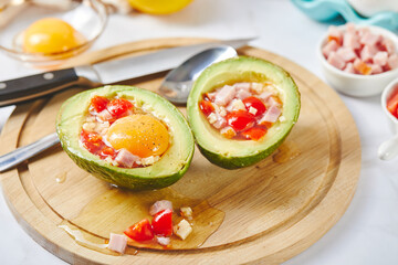 Wall Mural - Avocado with egg, ham, tomatoes and cheese. Keto lunch recipe. Before baking