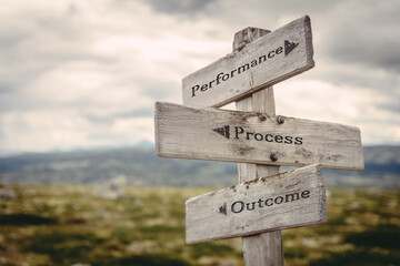 performance process outcome text quote written in wooden signpost outdoors in nature. Moody theme feeling.