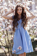 Canvas Print - beautiful woman with dark hair in elegant clothes posing in flowering park with magnolias