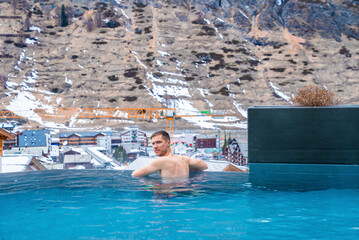 Wall Mural - Man enjoying in hot swimming pool against majestic mountain in alpine region