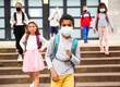© JackF - Portrait of schoolboy in medical mask standing near school, kids on background ..