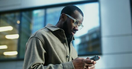 African-American man uses a mobile phone standing near a building in Evening