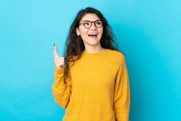 Teenager Russian girl isolated on blue background pointing up and surprised