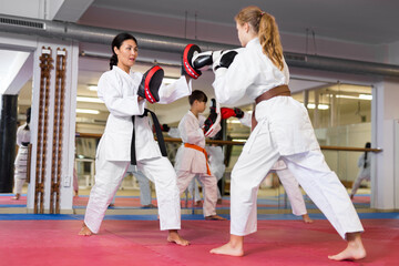 Focused girl practicing boxing punches in pair with her trainer during group mugendo course in gym