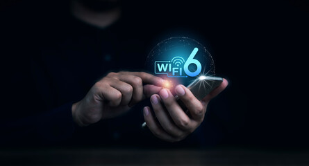 Wi-Fi 6 logo virtual appeared on mobile smartphone while business man's hand using it on dark background. New generation telecommunications connectivity network with smart performance.