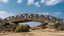 The Decorative Arch Bridge Is Made Of Palm Trunks. Lattice Railings Against A Background Of Blue Sky And Clouds. Boulders And Green Vegetation Are Visible On The Soil. Montazah Park. Alexandria. Egypt