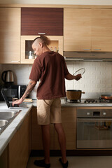 Young man in loungewear cooking soup for dinner and checking e-mails and notifications on laptop