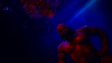 A Huge Bald Man With A Beard Demonstrates The Muscles Of Arms And Chest In Blue Water. Red Light. The Average Plan. The Camera Is Tilted